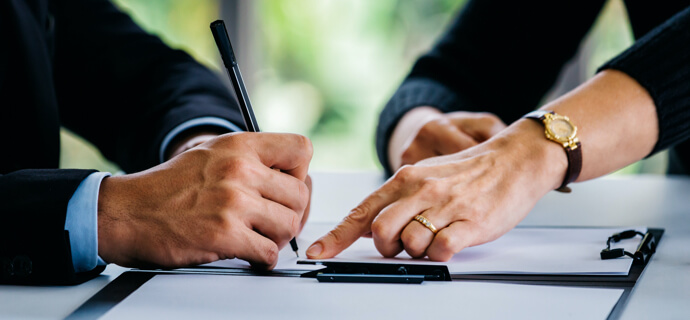 Side view of crop businesswoman pointing at contract to businessman with pen at table at office